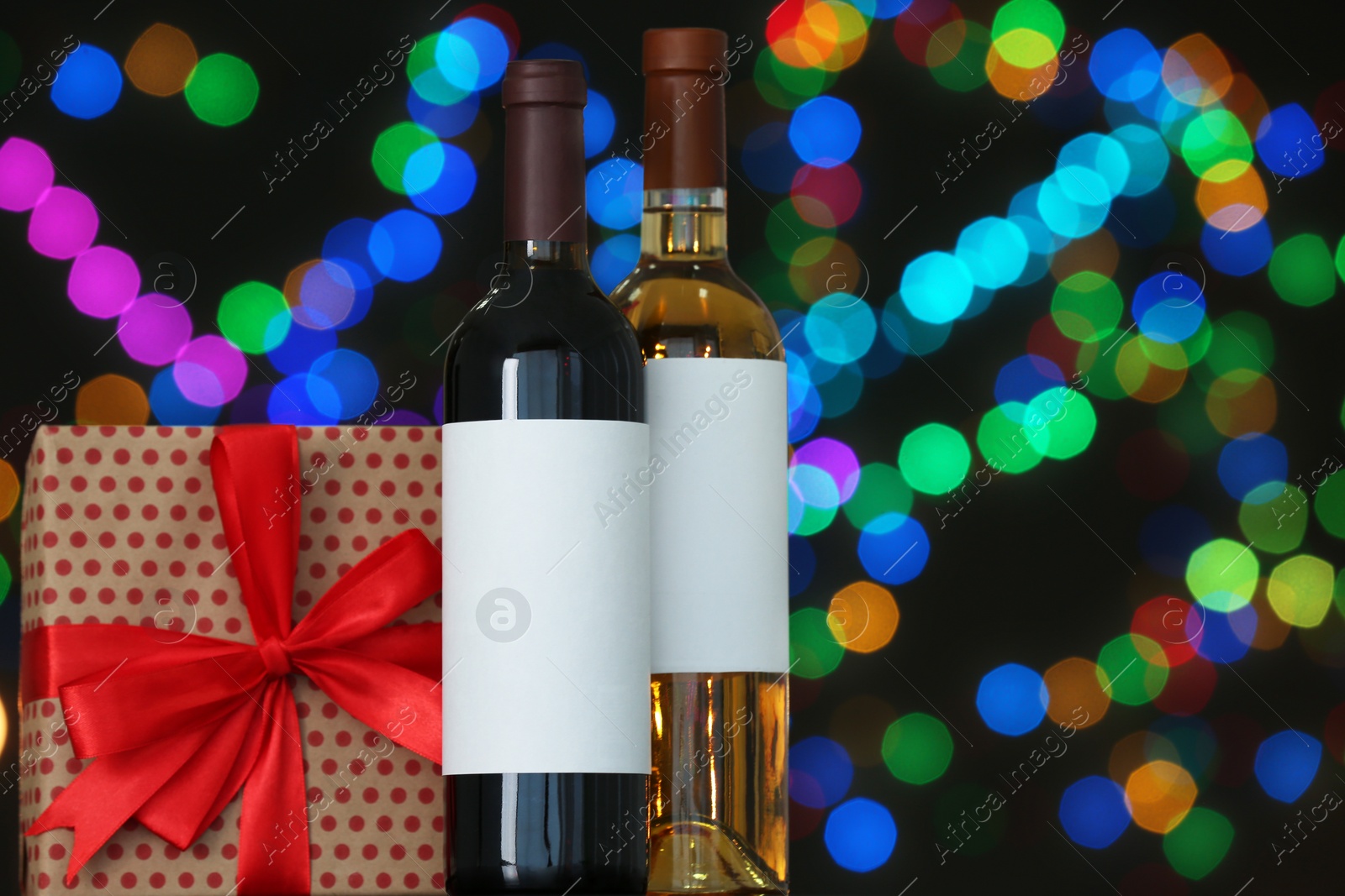 Photo of Gift box with and bottles of wine on table against blurred lights, space for text. Bokeh effect