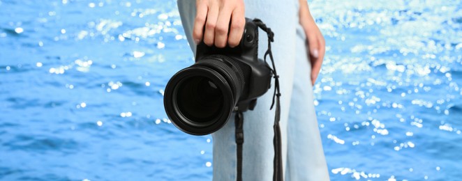 Professional photographer with modern camera and blurred view of beautiful sea on sunny day. Banner design