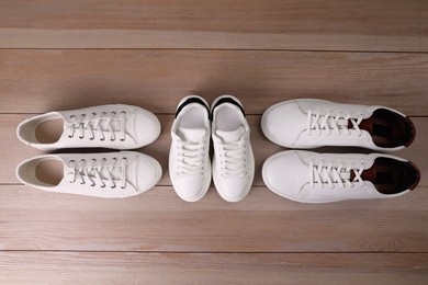 Stylish sports shoes for all family members on wooden floor, flat lay