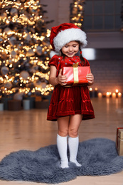 Cute little child wearing Santa hat with Christmas gift in living room