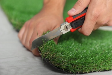 Man cutting artificial grass carpet indoors, closeup