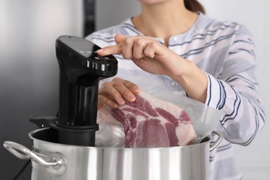 Photo of Woman putting vacuum packed meat into pot and using thermal immersion circulator, closeup. Sous vide cooking