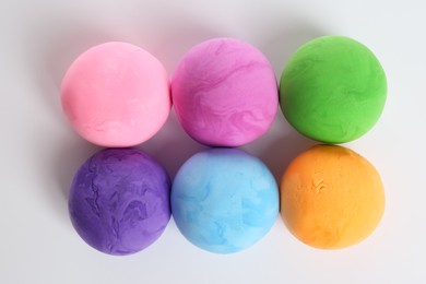 Different color play dough balls on white background, top view