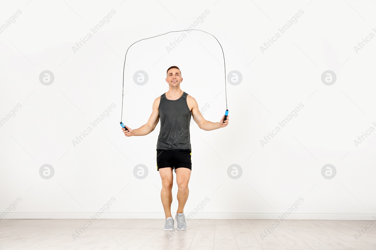 Photo of Full length portrait of young sportive man training with jump rope in light room