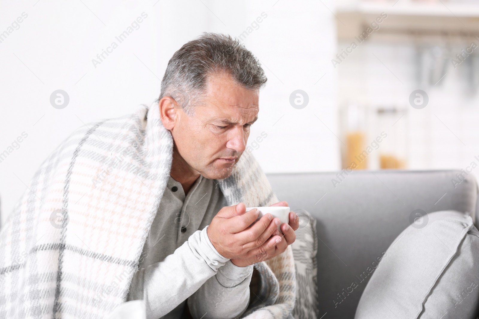 Photo of Man with cup of tea for cough on sofa at home