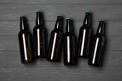 Glass bottles of beer on grey wooden background, flat lay
