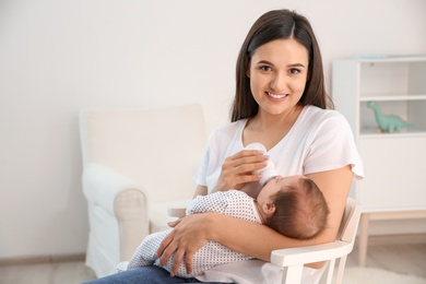 Photo of Woman feeding her baby from bottle in nursery at home. Space for text