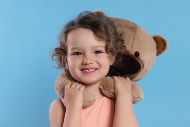 Cute little girl with teddy bear on light blue background