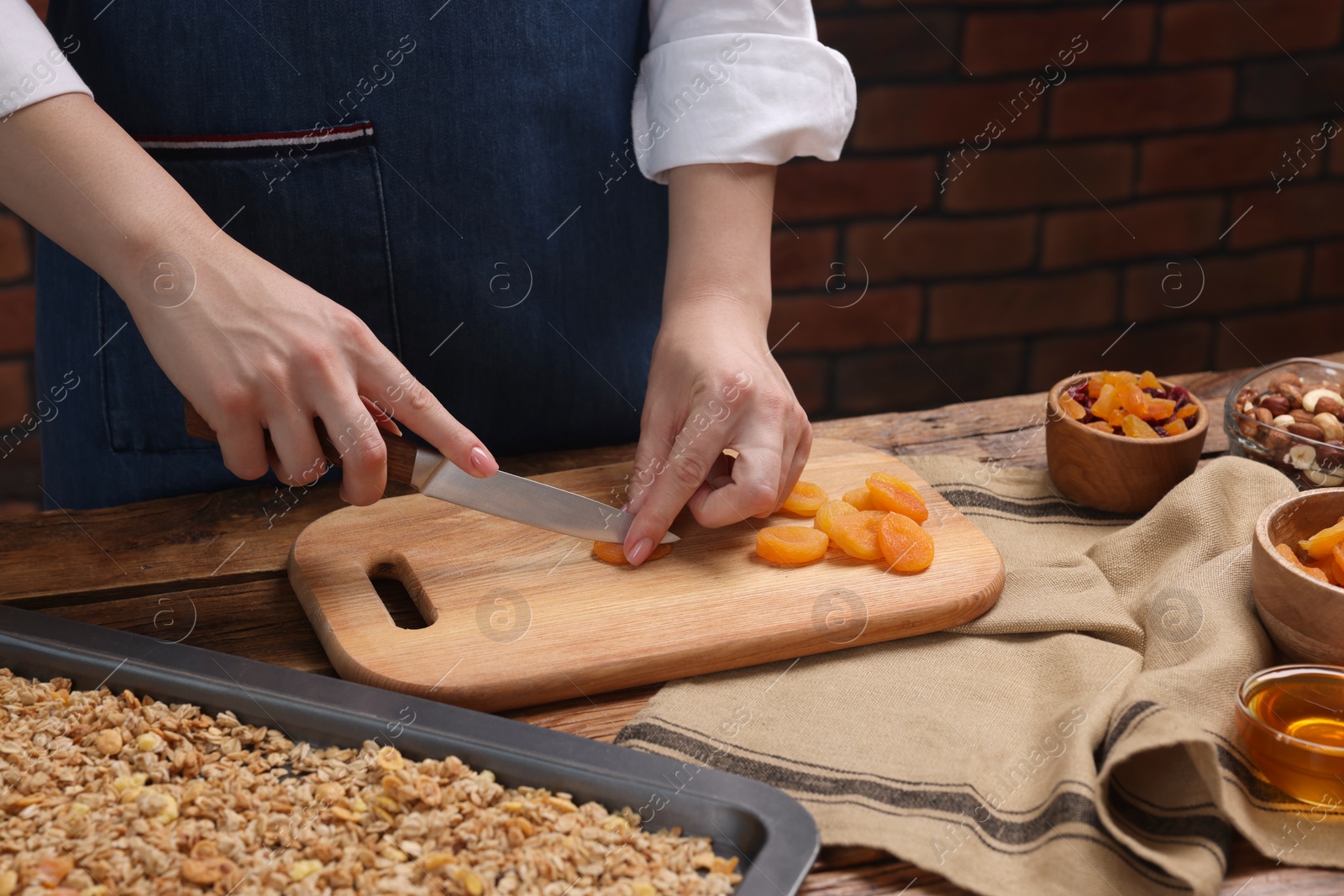 Photo of Making granola. Woman cutting dry apricots at wooden table, closeup