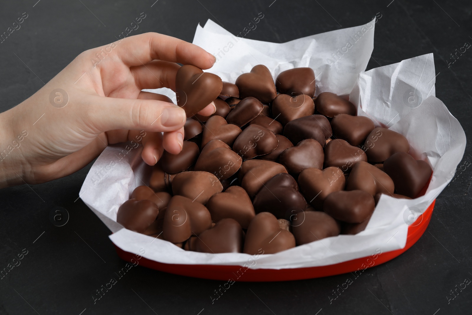 Photo of Woman with box of heart shaped chocolate candies at black table, closeup