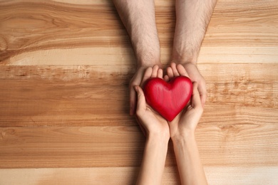 Couple holding decorative heart on wooden background, top view