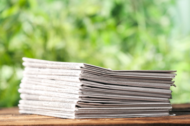 Stack of newspapers on wooden table against blurred green background. Journalist's work