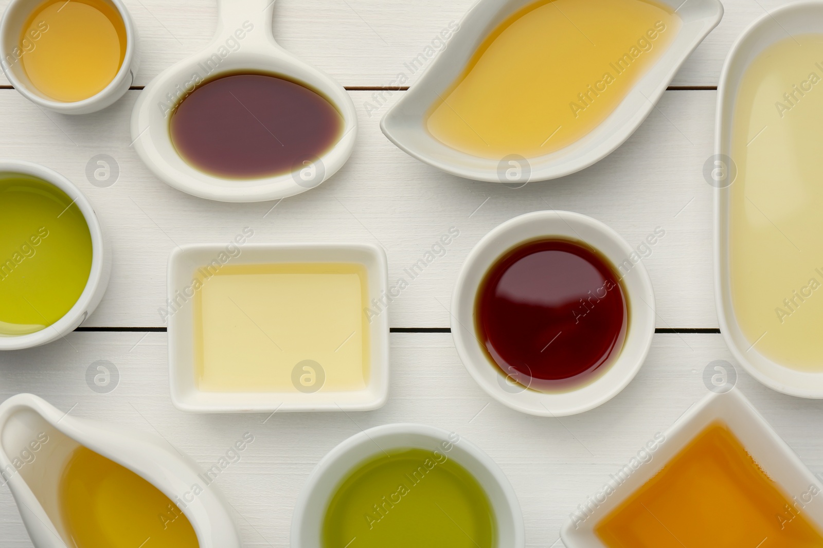 Photo of Vegetable fats. Different cooking oils on white wooden table, flat lay