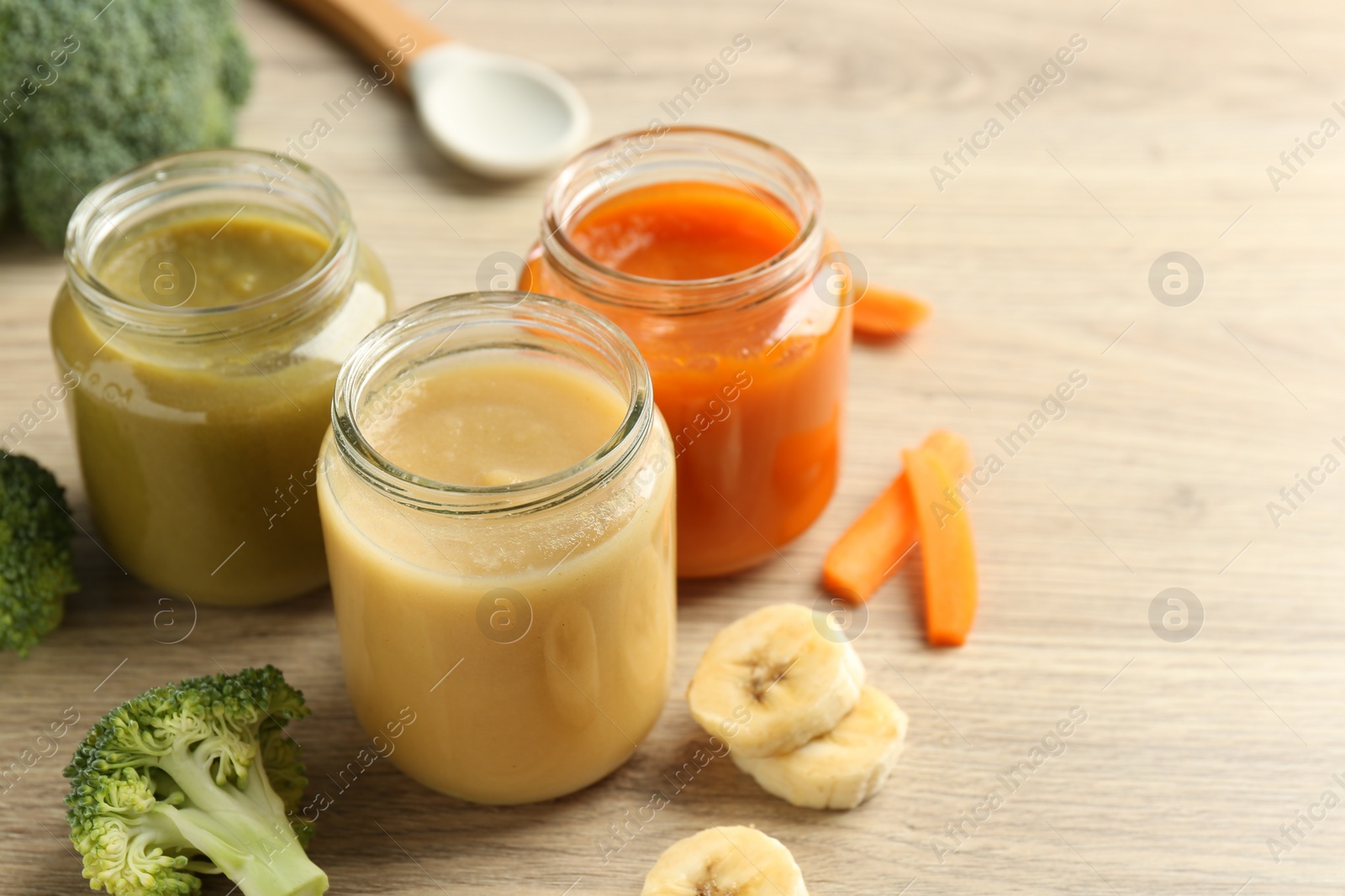 Photo of Tasty baby food in jars and ingredients on light wooden table, space for text
