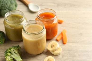 Tasty baby food in jars and ingredients on light wooden table, space for text