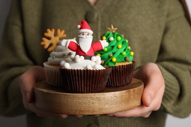 Photo of Woman holding board with tasty Christmas cupcakes, closeup