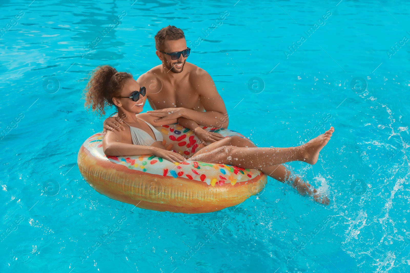 Photo of Happy couple with inflatable ring in outdoor swimming pool on sunny summer day