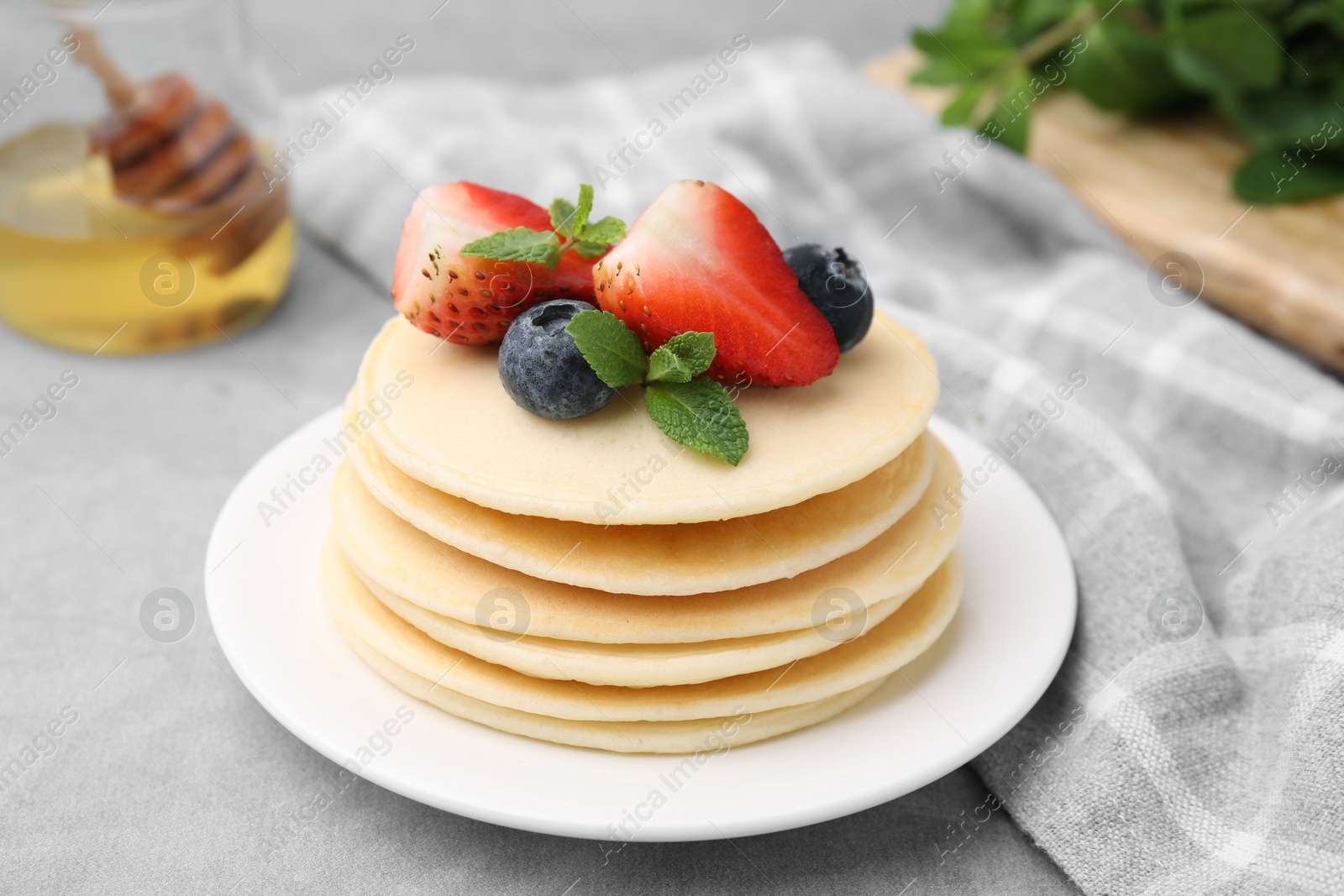 Photo of Stack of tasty pancakes with fresh berries and mint on light grey table, closeup