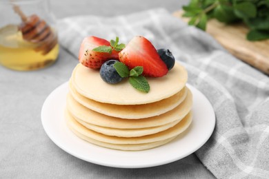 Stack of tasty pancakes with fresh berries and mint on light grey table, closeup