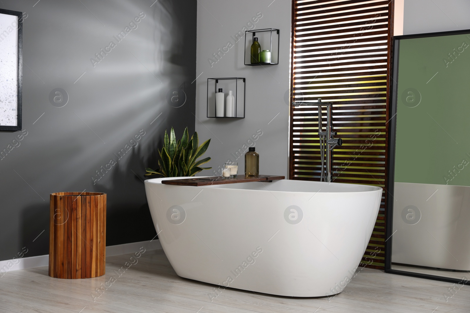 Photo of Stylish bathroom interior with ceramic tub, candles and care products on wooden bath tray