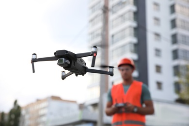 Builder operating drone with remote control at construction site, focus on quadcopter. Aerial survey