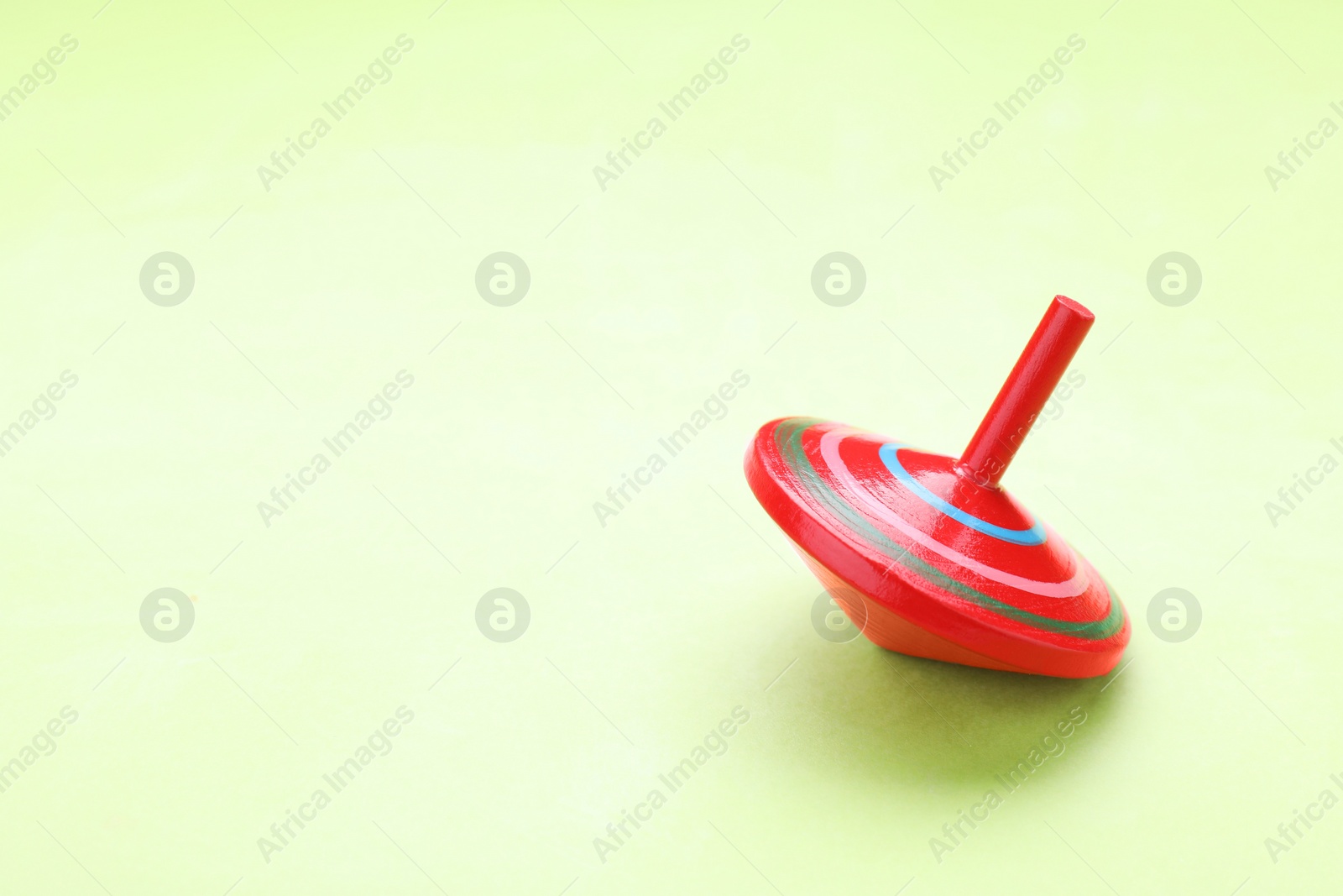 Photo of One bright spinning top on light green background, space for text. Toy whirligig