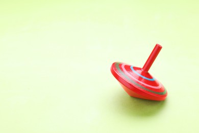 Photo of One bright spinning top on light green background, space for text. Toy whirligig