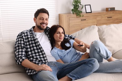 Photo of Happy couple watching show at home. Woman changing TV channels with remote control