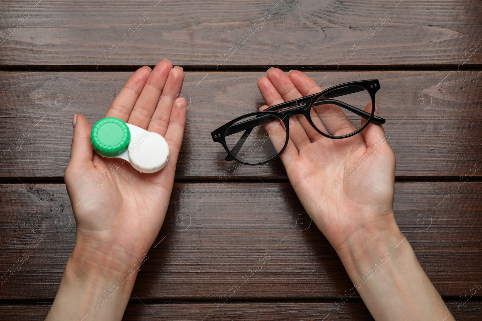 Photo of Woman holding case with contact lenses and glasses at wooden table, top view