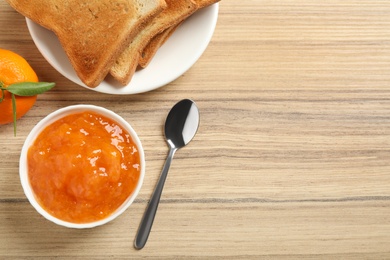 Tasty jam, toasts and fresh tangerine on wooden table, flat lay. Space for text