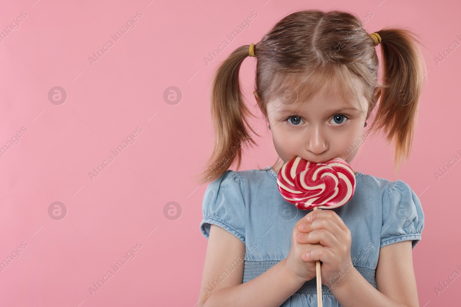 Photo of Portrait of cute girl licking lollipop on pink background, space for text