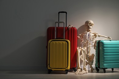 Waiting concept. Human skeleton with suitcases near grey wall, space for text