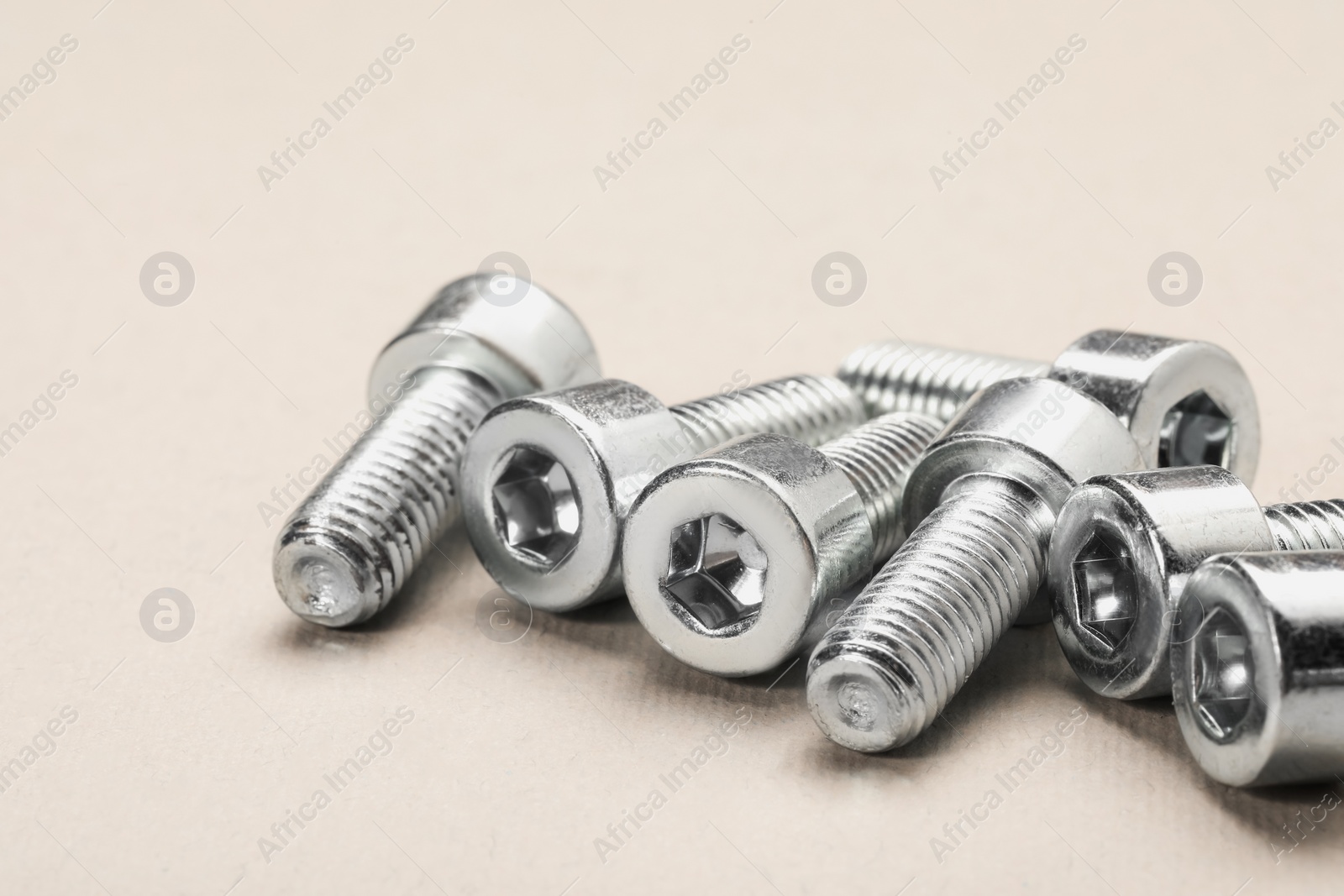 Photo of Many metal socket screws on beige background, closeup