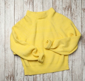 Beautiful yellow warm sweater on white wooden table, top view