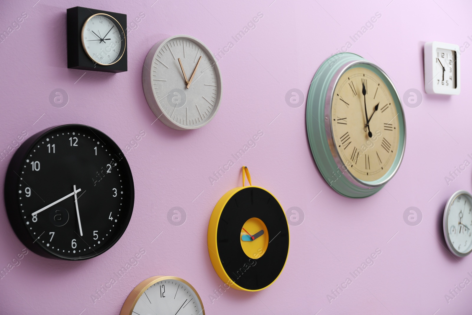 Photo of Many different clocks hanging on color wall. Time of day