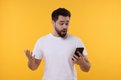 Shocked young man using smartphone on yellow background