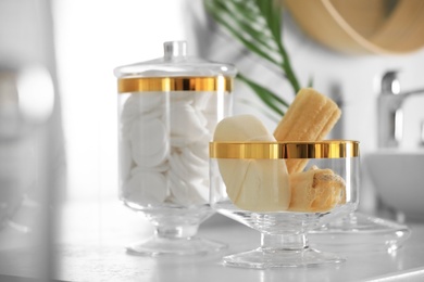 Jars with cotton pads and loofah sponges on countertop in bathroom