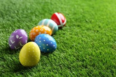 Colorful painted Easter eggs on green grass, space for text
