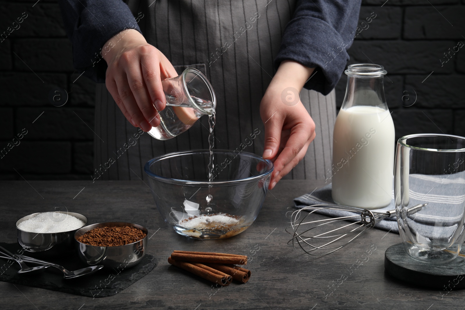 Photo of Making dalgona coffee. Woman pouring water into bowl at grey table, closeup