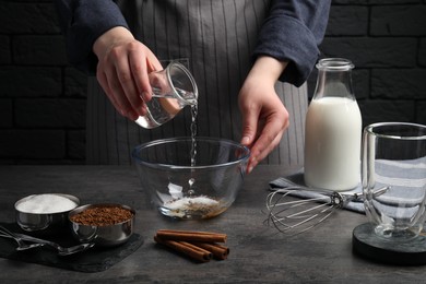 Making dalgona coffee. Woman pouring water into bowl at grey table, closeup