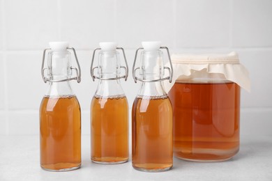 Tasty kombucha in glass jar and bottles on white table