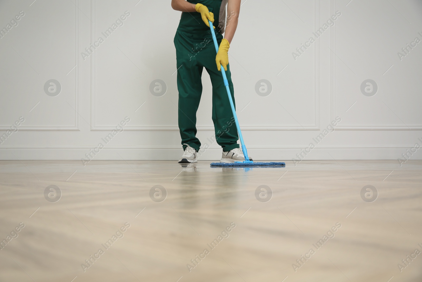 Photo of Professional janitor cleaning parquet floor with mop indoors, closeup