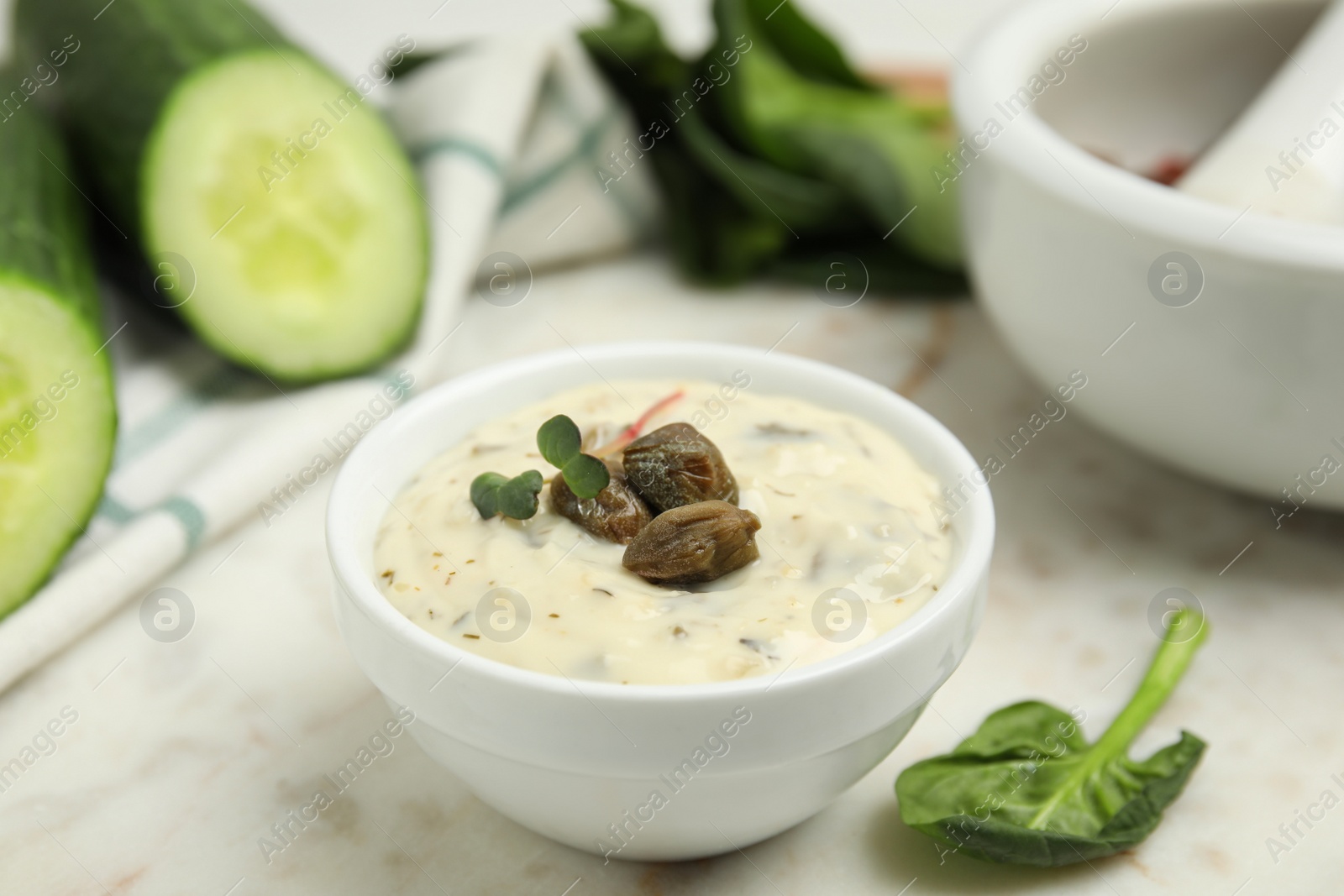 Photo of Creamy caper sauce in bowl on white marble table, closeup