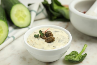 Creamy caper sauce in bowl on white marble table, closeup