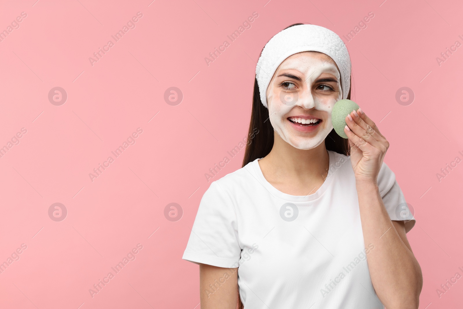 Photo of Young woman with headband washing her face using sponge on pink background, space for text