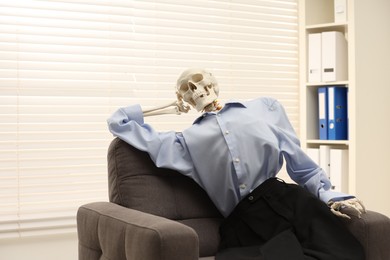 Waiting concept. Human skeleton sitting in armchair at office