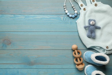 Cute knitted baby bodysuit, booties and toys on light blue wooden background, flat lay. Space for text