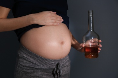 Photo of Pregnant woman with bottle of whiskey on dark background. Alcohol addiction