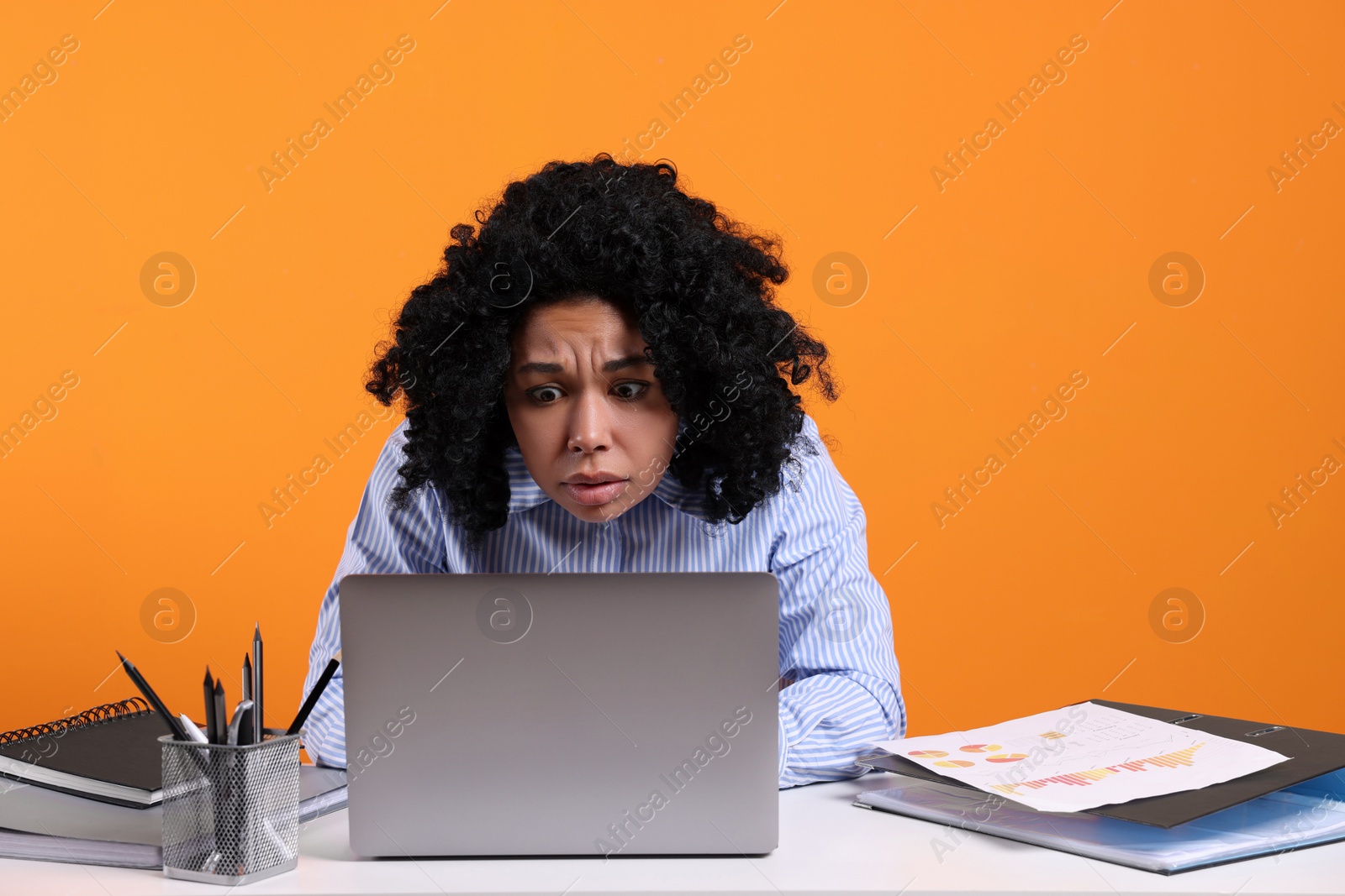 Photo of Stressful deadline. Sad woman looking at laptop at white table on orange background