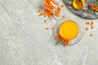 Delicious sea buckthorn tea and fresh berries on grey table, flat lay. Space for text